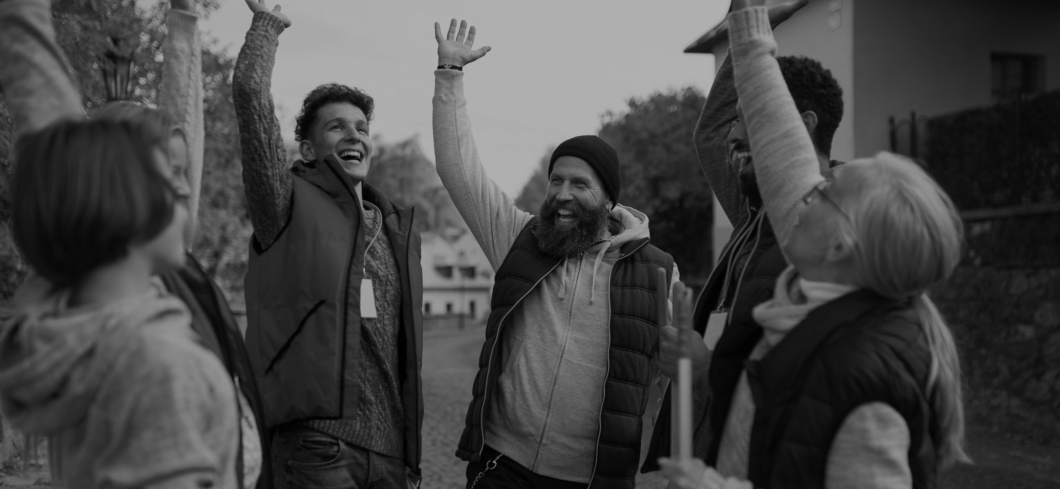 A group of people of different ages cheering with hands raised, some holding cleaning tools, celebrating after a community clean-up.